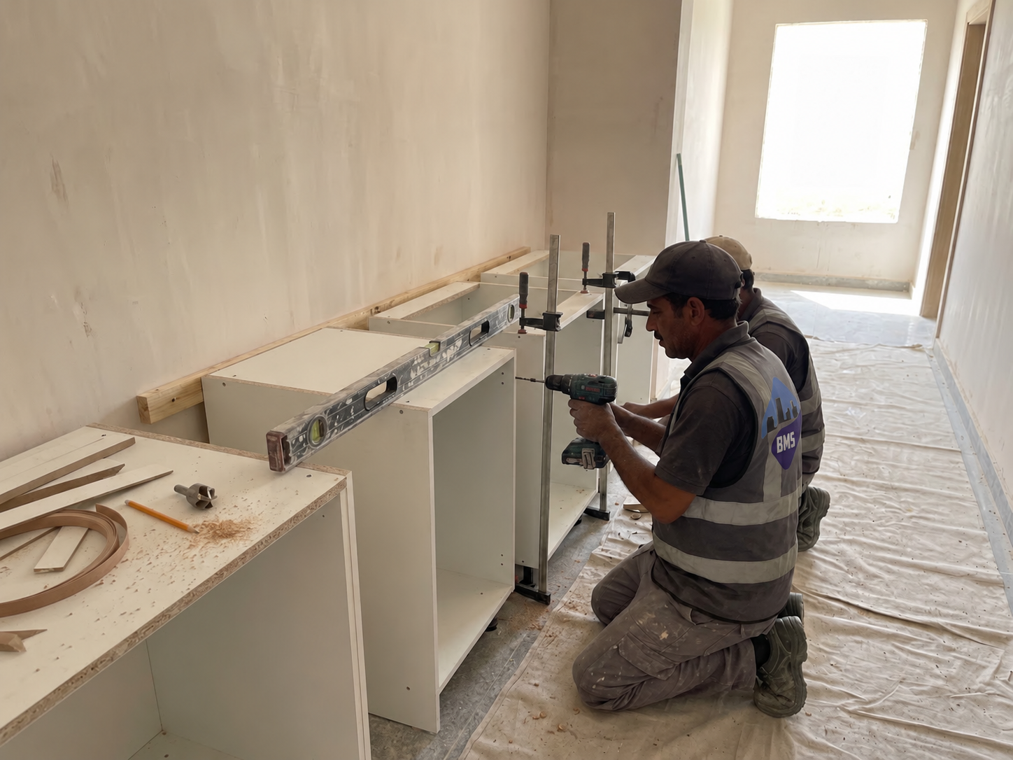 Carpenter fixing a run of custom cabinetry carcasses to the wall