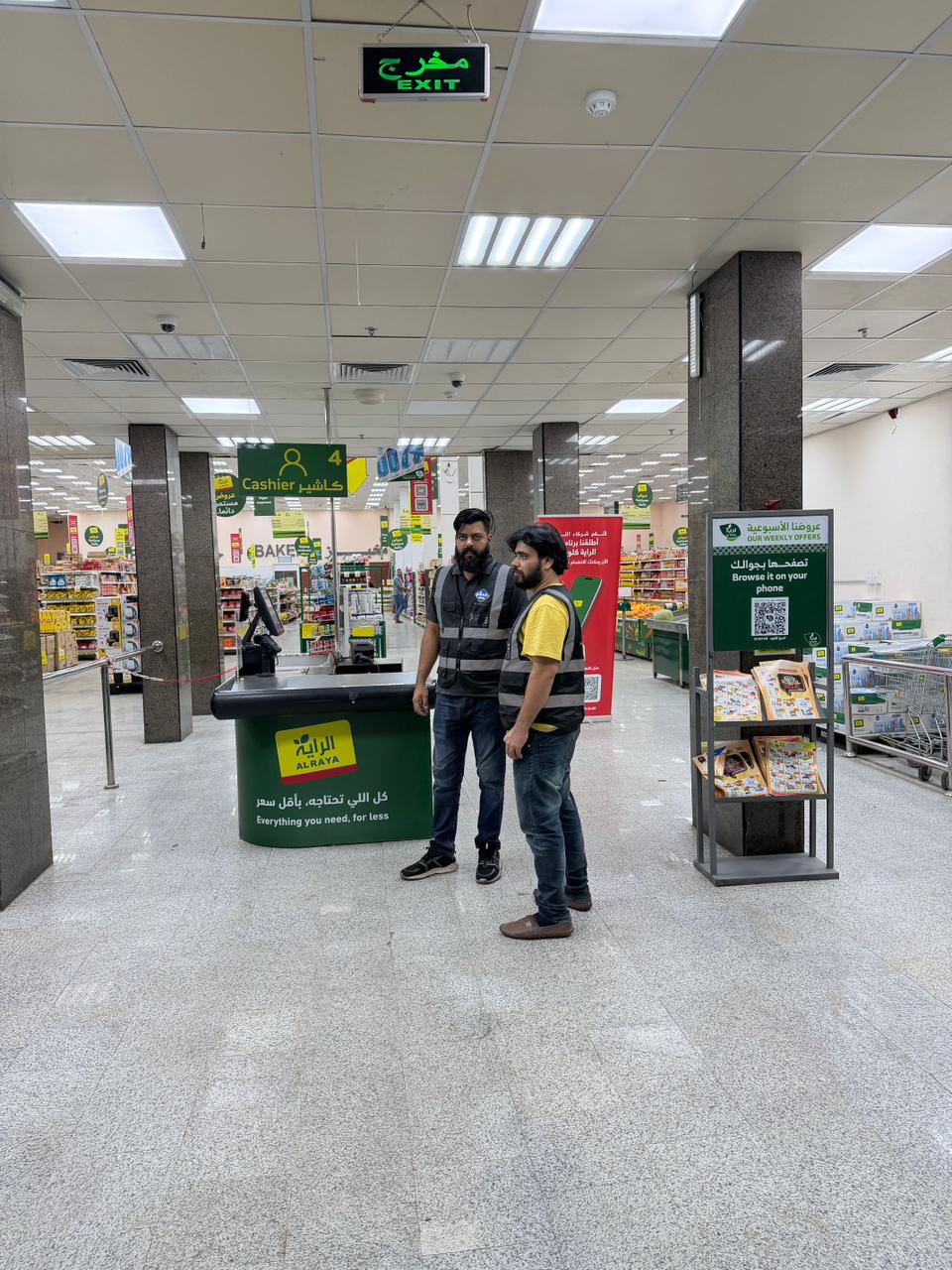 Two BMS technicians on the sales floor beside a supermarket checkout counter