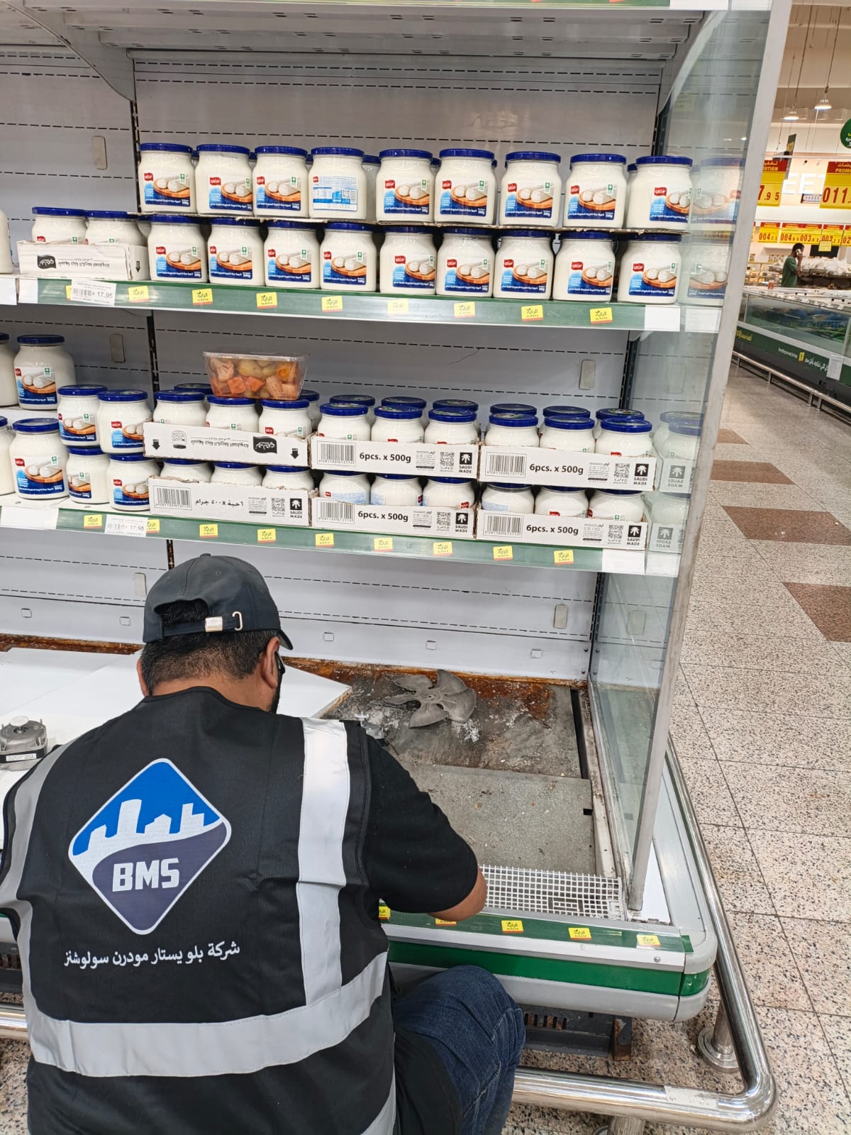 BMS technician working on an evaporator fan at the open base of a supermarket display fridge