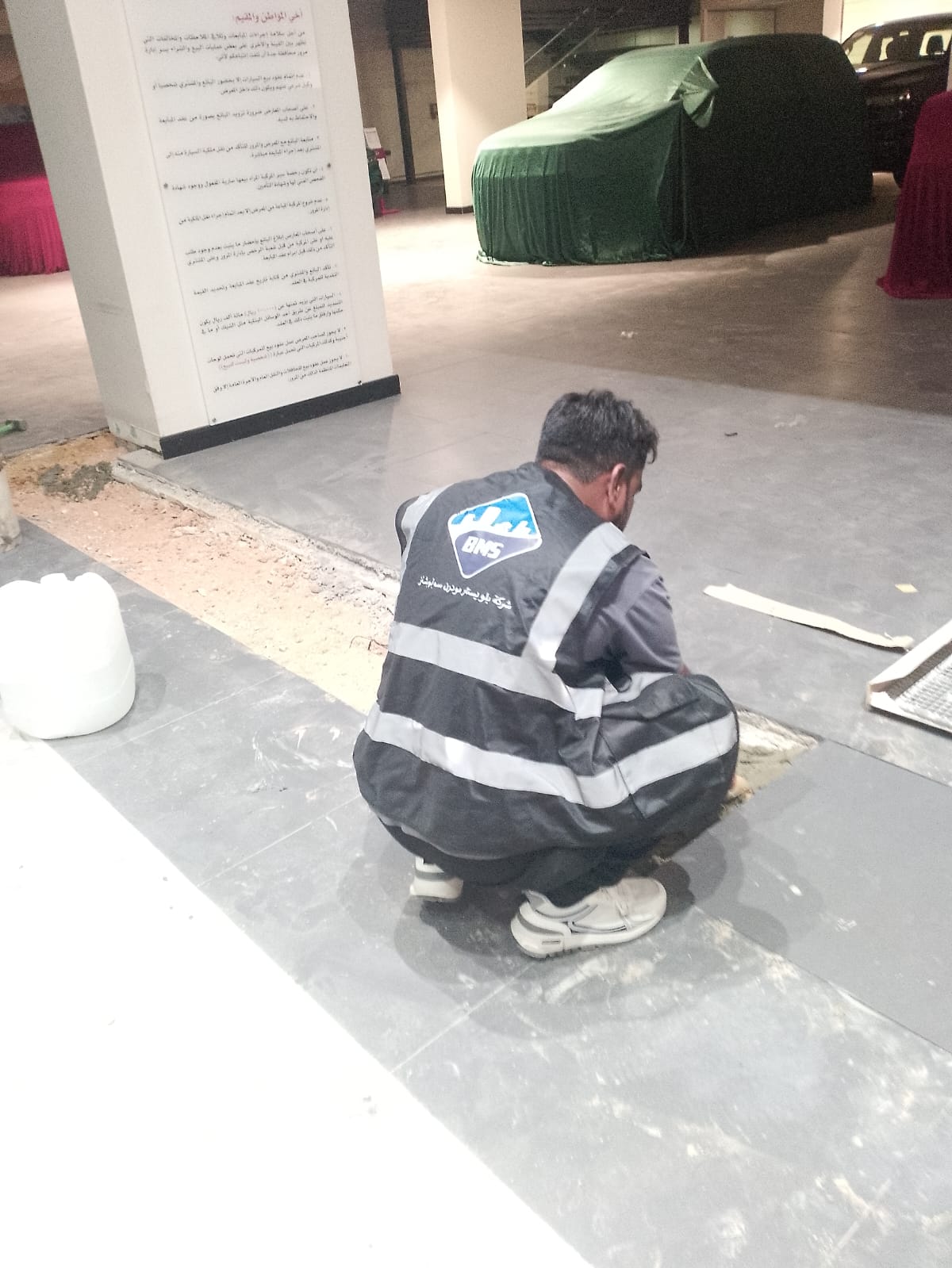 BMS technician repairing floor tiling and screed in a commercial showroom