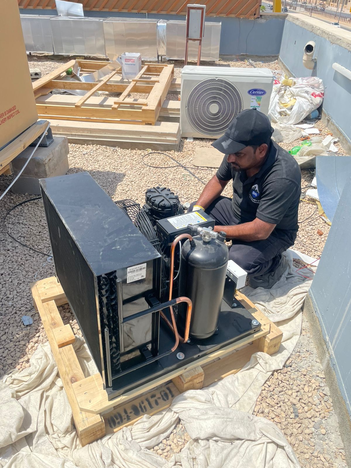 BMS technician preparing an unpacked refrigeration condensing unit on the rooftop plant deck