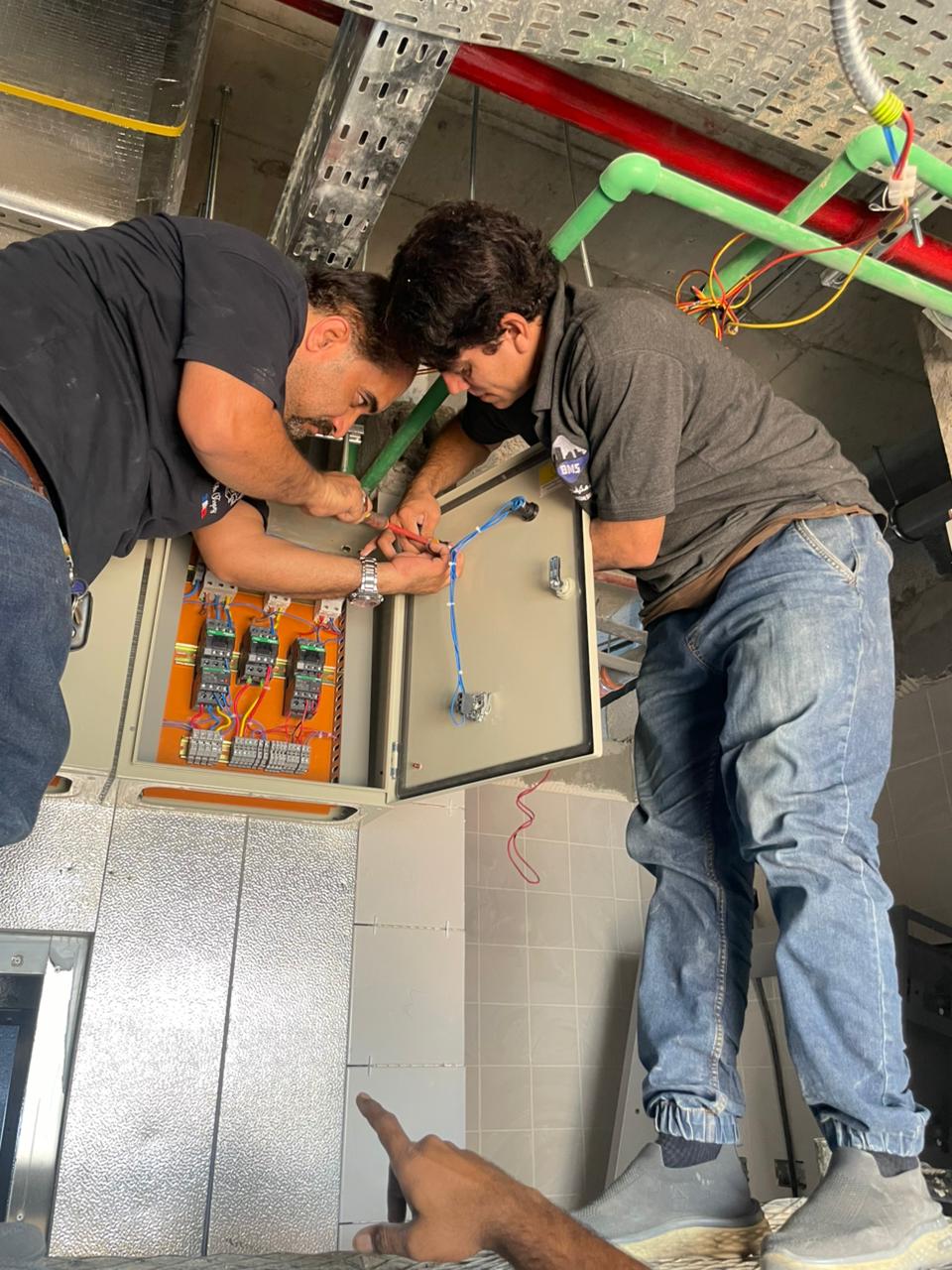 Two BMS technicians terminating cables inside an electrical control panel