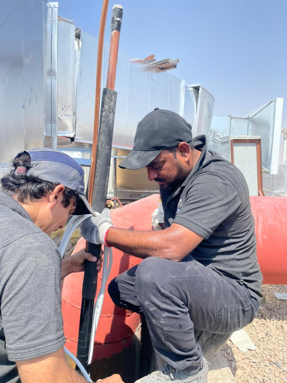 Two BMS technicians fitting insulation to a copper suction line on the rooftop