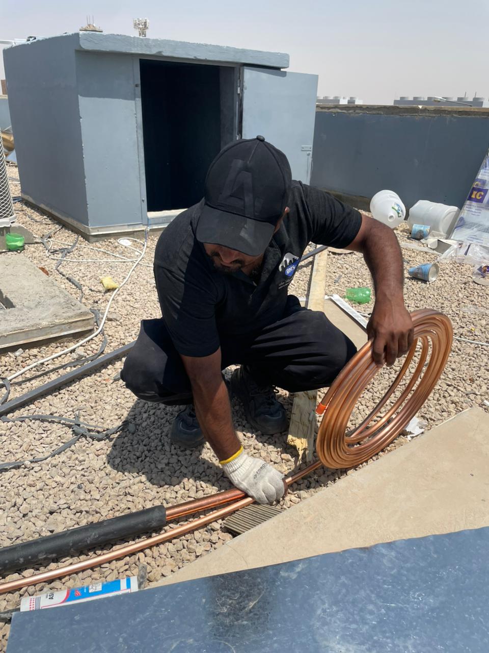BMS technician uncoiling copper refrigerant pipe on the roof ahead of installation