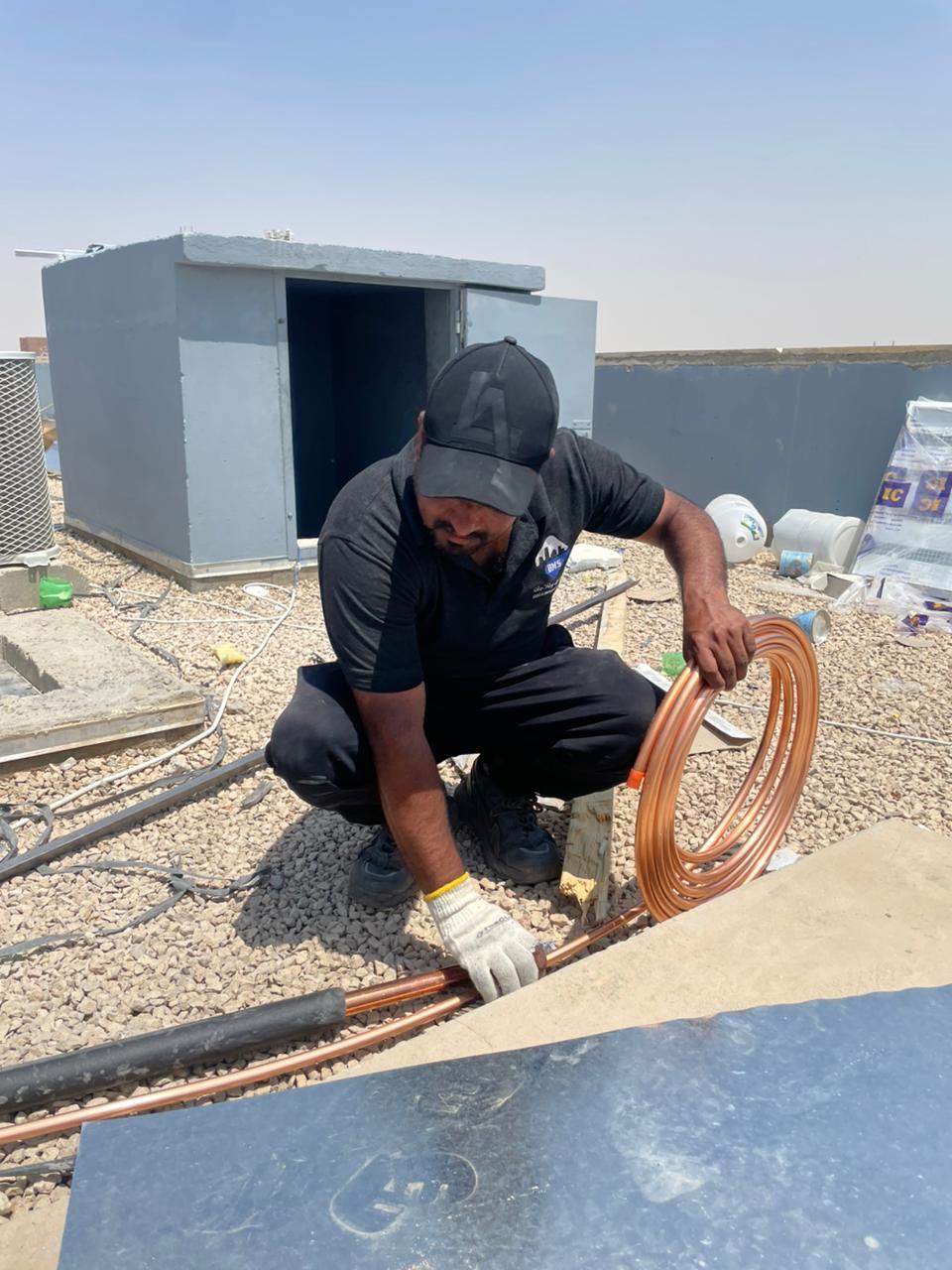 BMS technician uncoiling copper refrigerant tube on the roof beside the plant enclosure