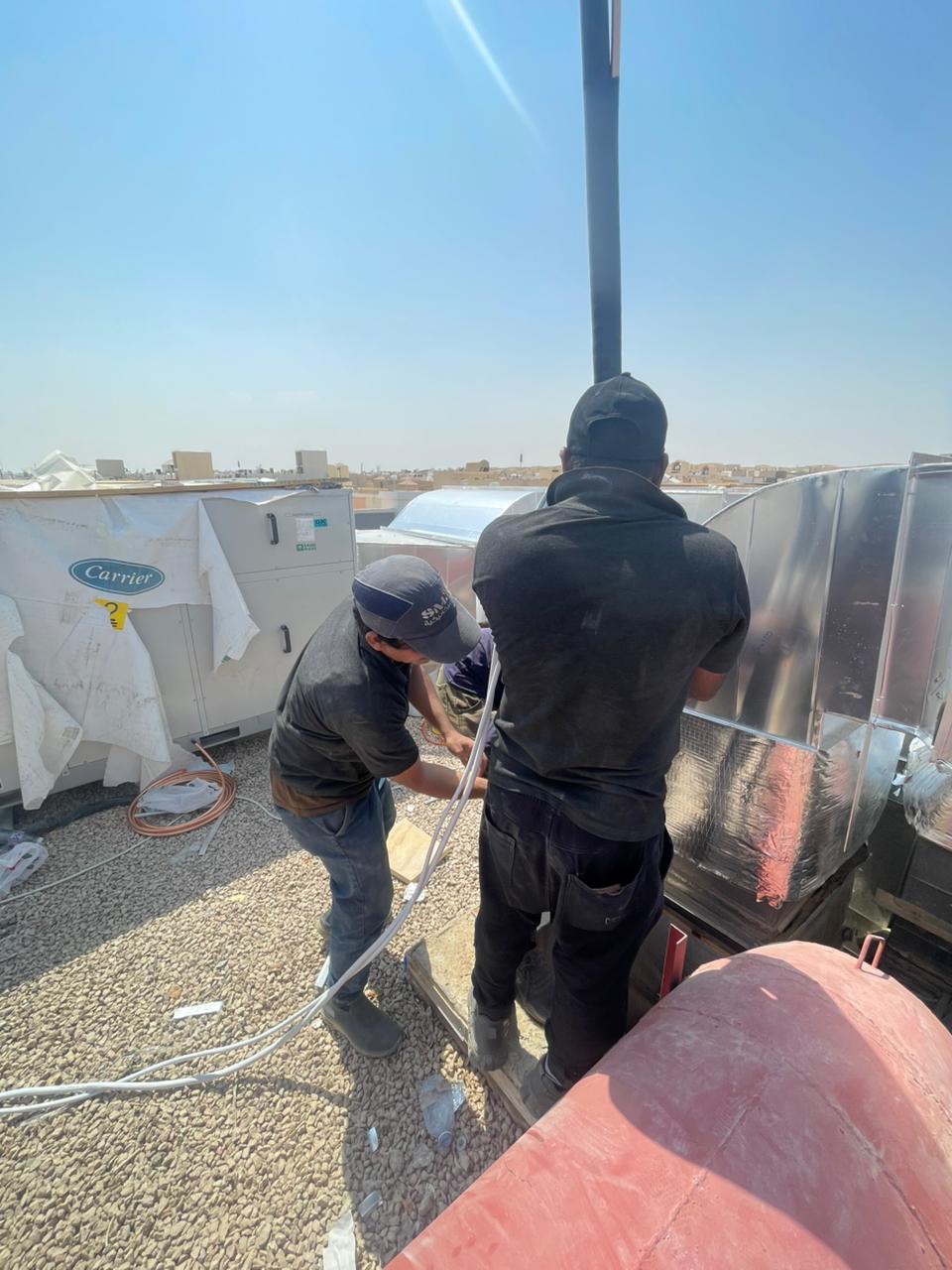 BMS technicians installing rooftop ductwork alongside a Carrier air-handling unit