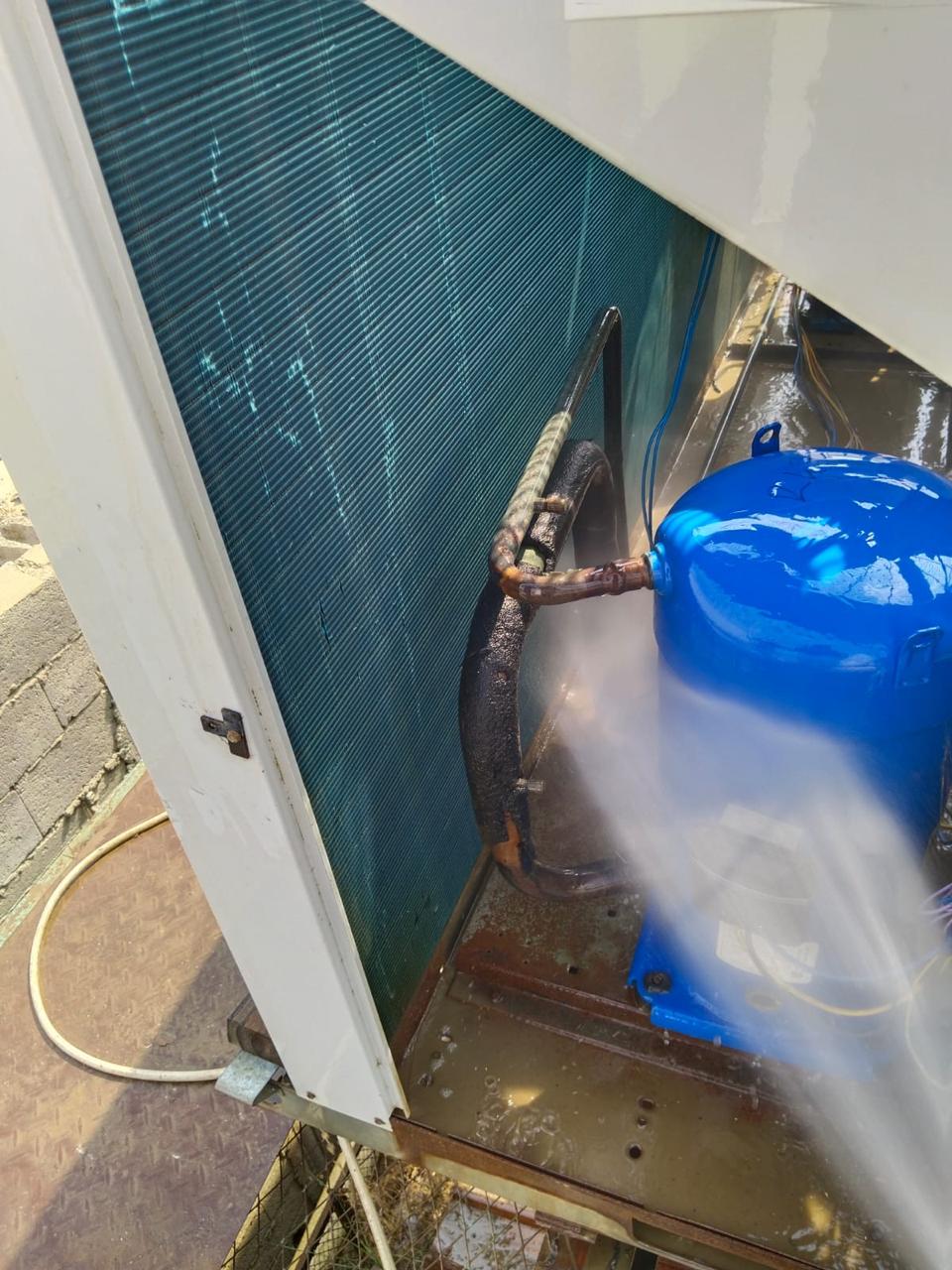 Water jet washing the finned condenser coil inside an opened outdoor unit housing